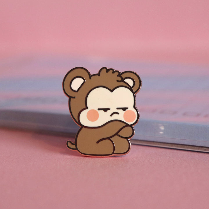 Grumpy monkey enamel pin on pink table with notepad