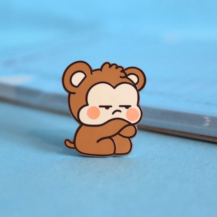 Grumpy monkey enamel pin on blue table with notepad