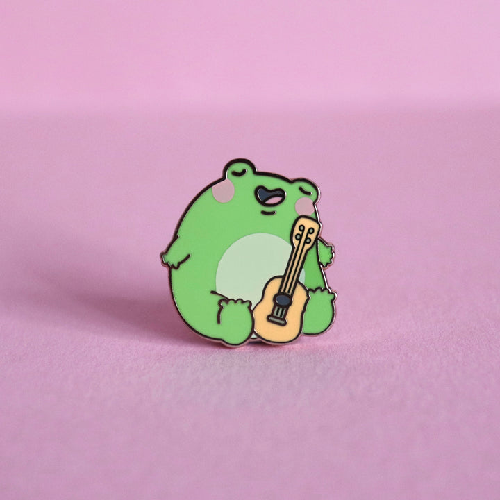 Frog with guitar enamel pin on pink table