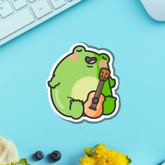 Frog playing guitar vinyl sticker on blue table with keyboard