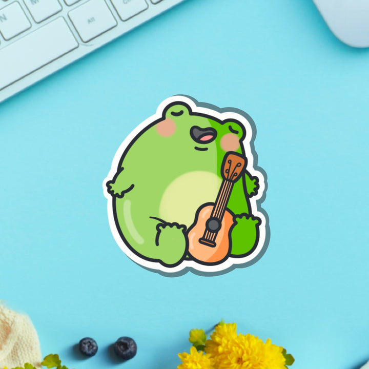 Frog playing guitar vinyl sticker on blue table with keyboard