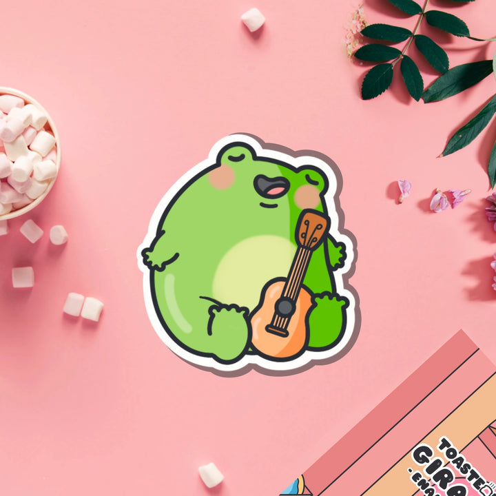 Frog playing guitar vinyl sticker on pink table