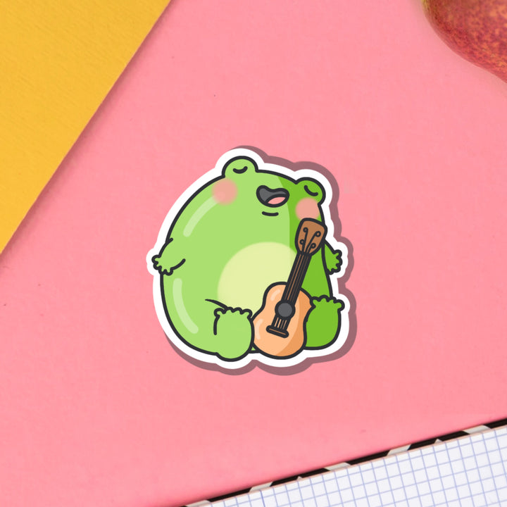 Frog playing guitar vinyl sticker on pink table