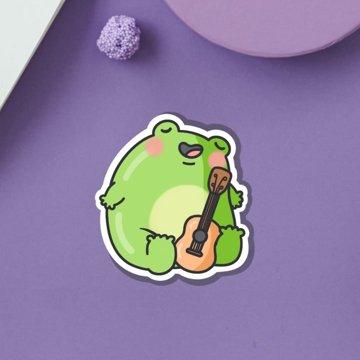 Frog playing guitar vinyl sticker on purple table