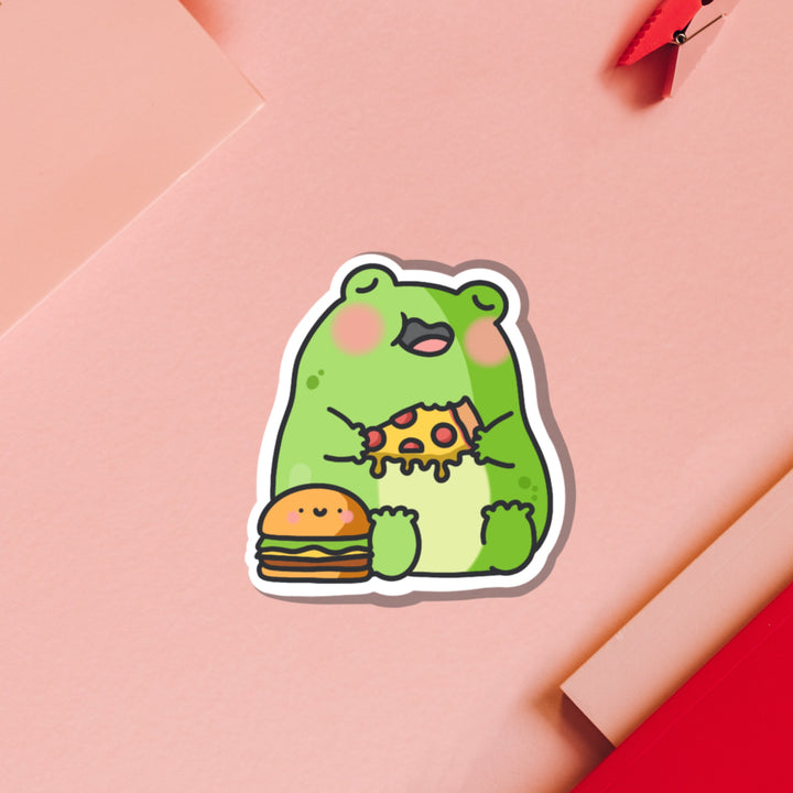 Frog eating pizza vinyl sticker on pink table with notebook