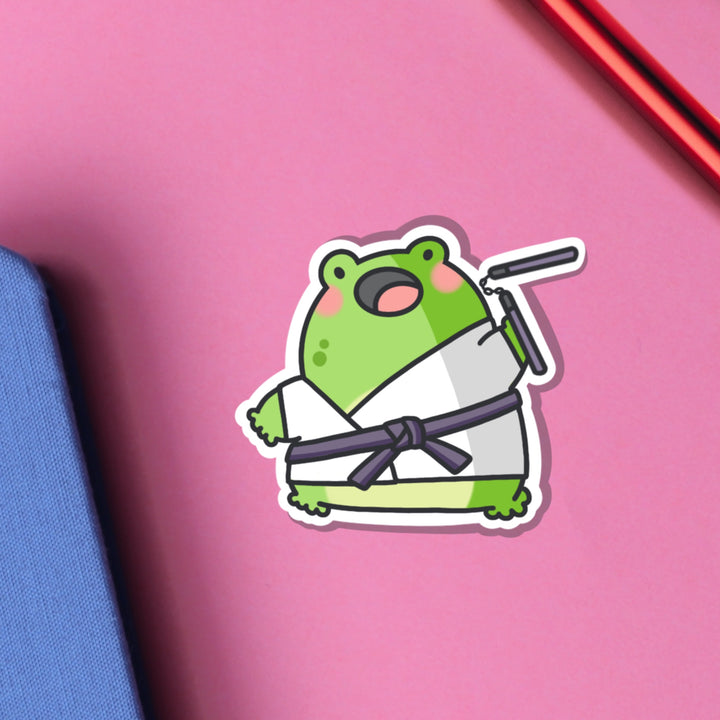 Karate frog vinyl sticker on pink table and notebook