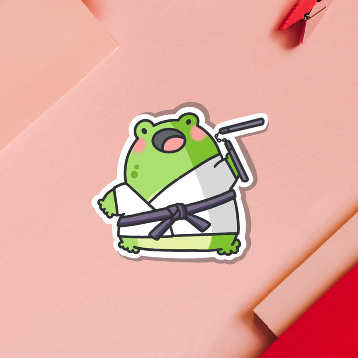 Karate frog vinyl sticker on pink table and notebook