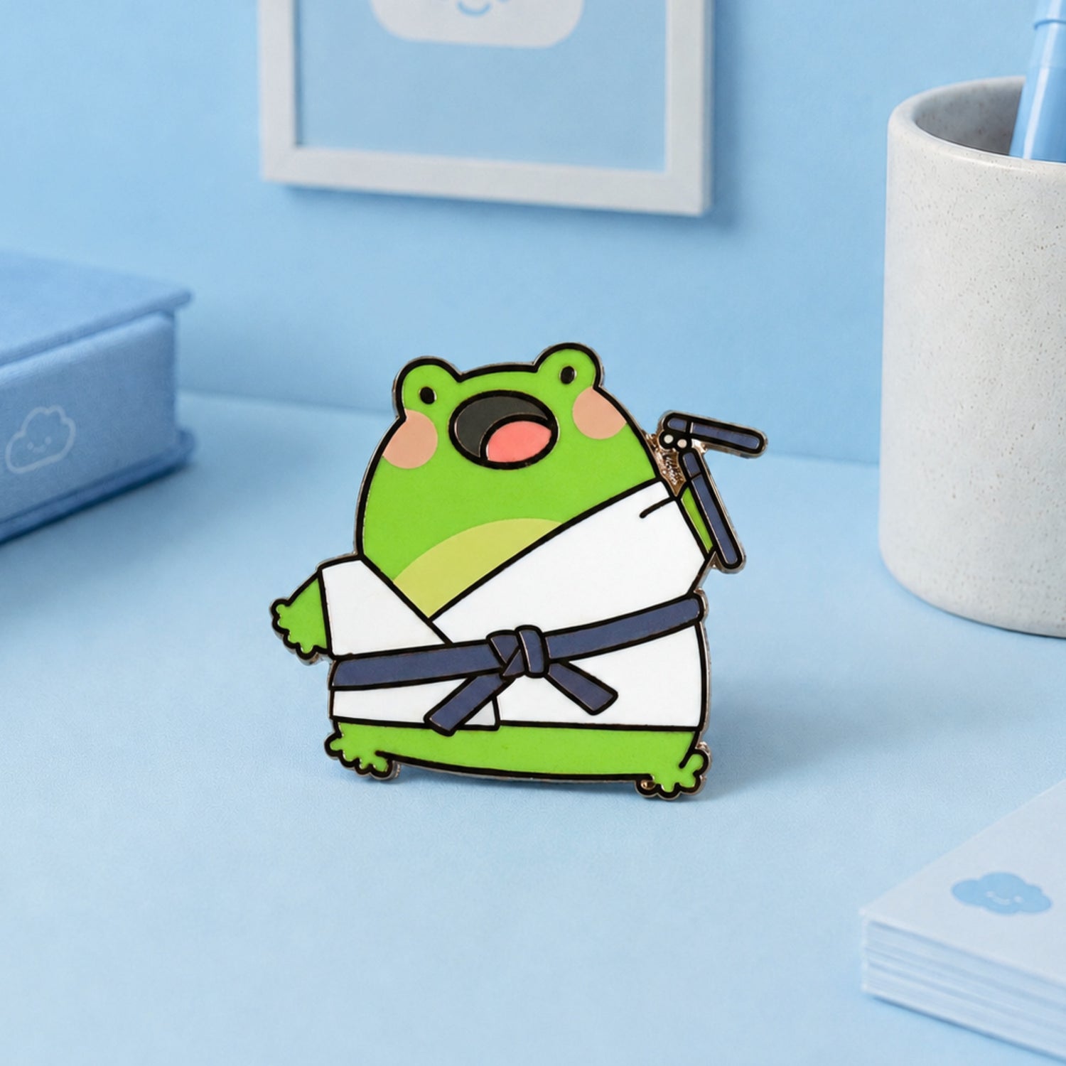 Karate frog enamel pin on blue desk with stationery