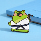 Cute karate frog enamel pin on blue table with notepad
