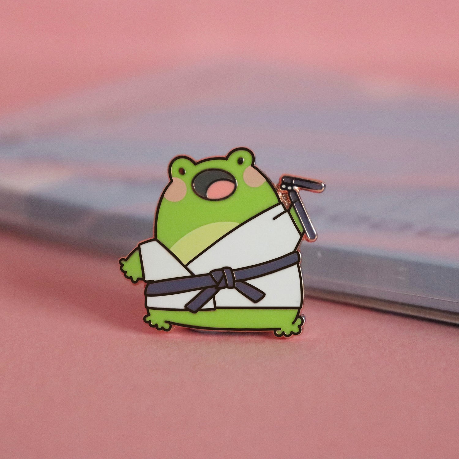Karate frog enamel pin on pink table with notepad