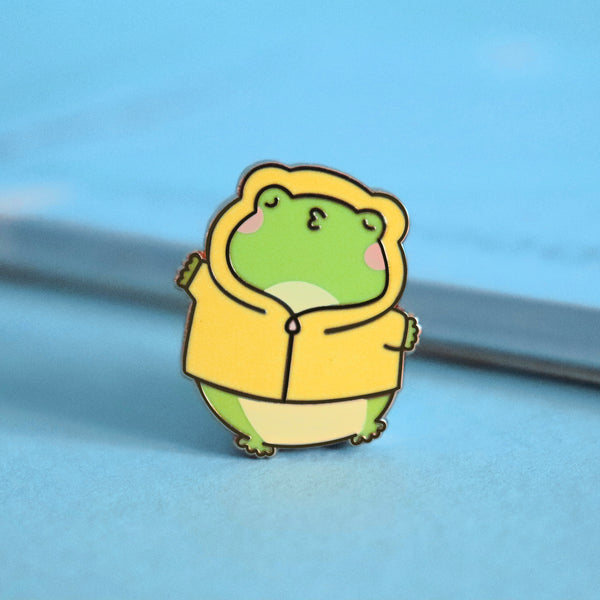 Kissing frog enamel pin on blue table with notepad