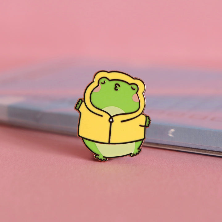 Kissing frog enamel pin on pink table with notepad