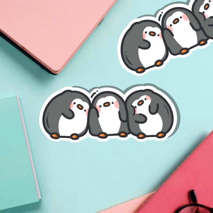 Three penguins in a line vinyl sticker on green table with notebook