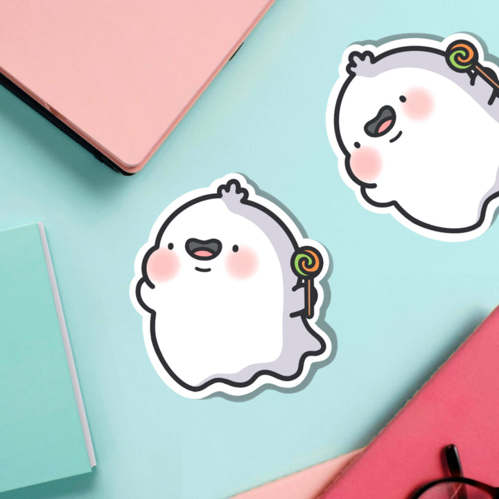 Ghost holding lollipop vinyl sticker on green table with notebooks