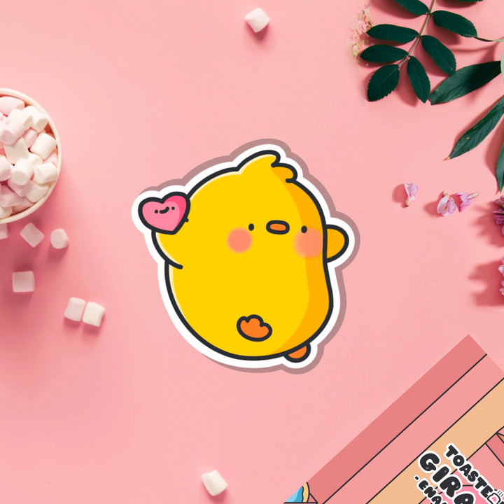 Chick holding love heart vinyl sticker on pink table