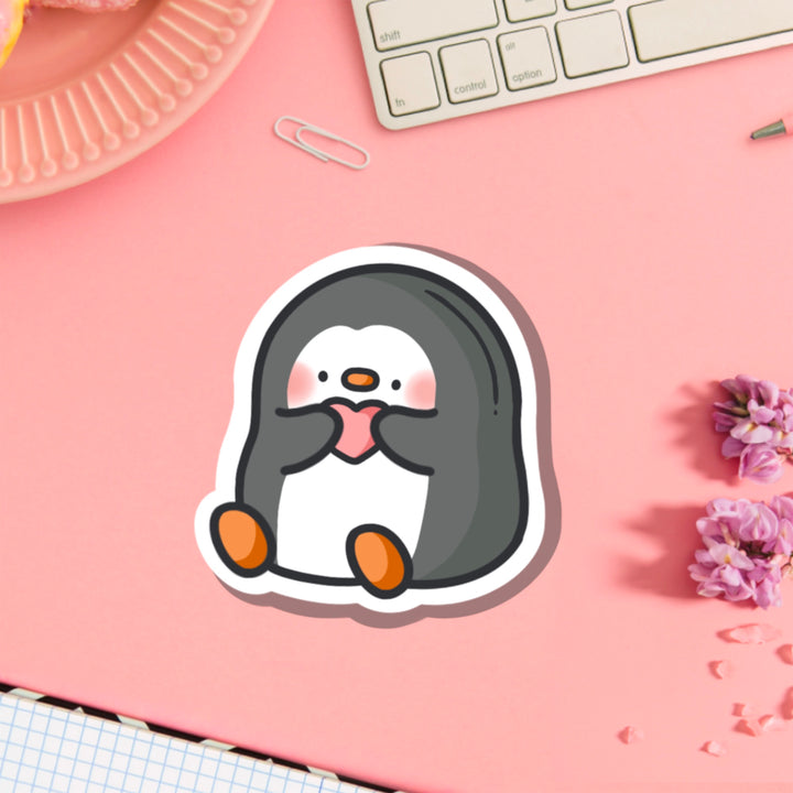 Penguin holding love heart vinyl sticker on pink table