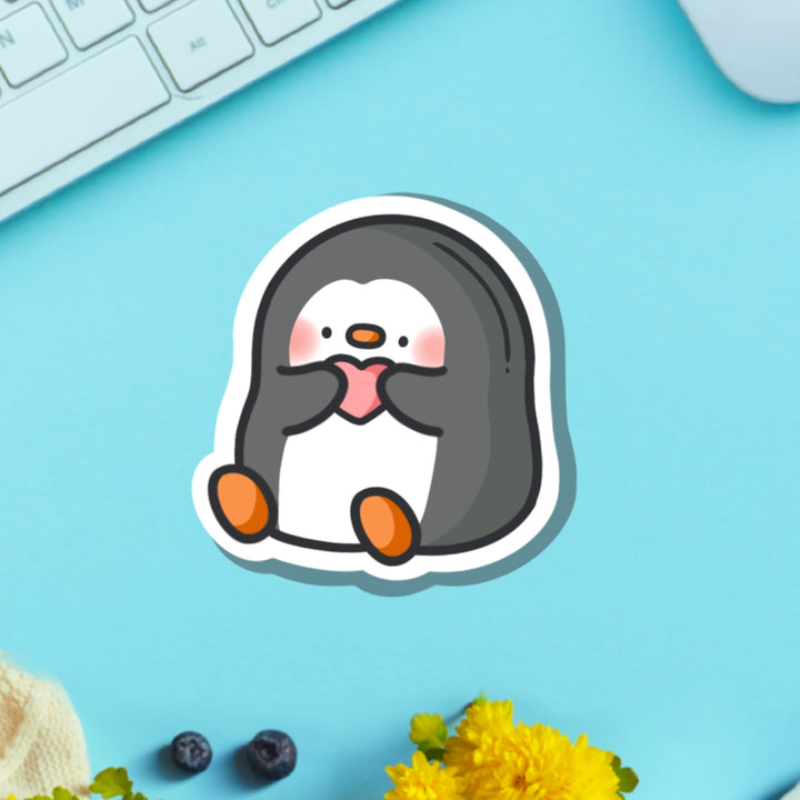 Penguin holding love heart vinyl sticker on blue table with keyboard