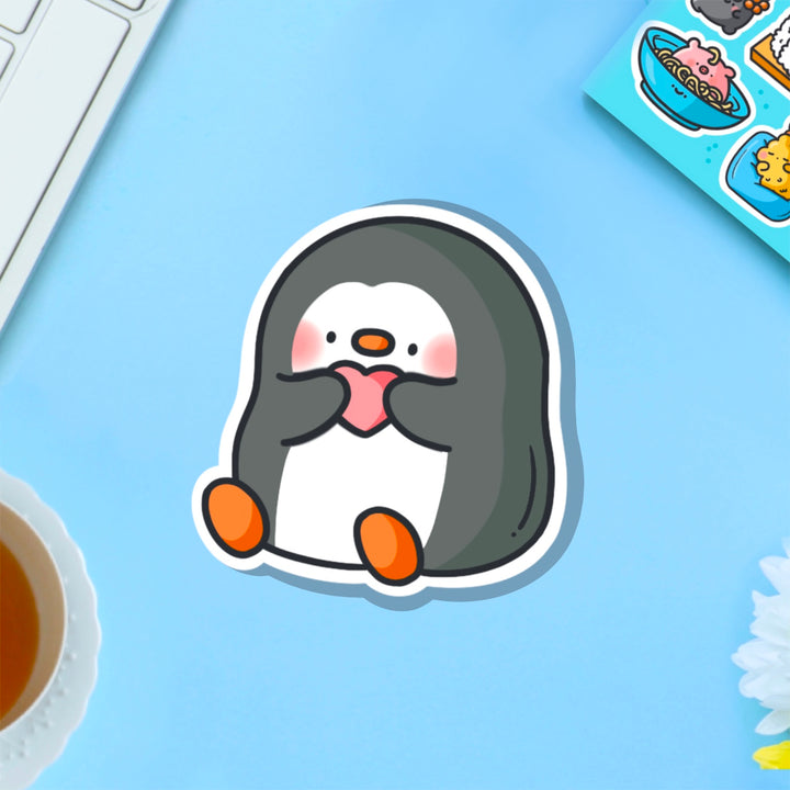 Penguin holding heart vinyl sticker on blue table