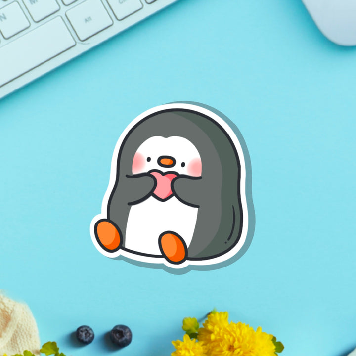 Penguin holding heart vinyl sticker on blue table with keyboard