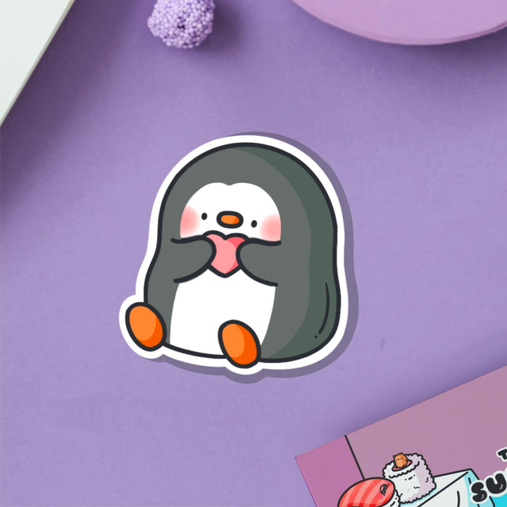 Penguin holding heart vinyl sticker on purple table