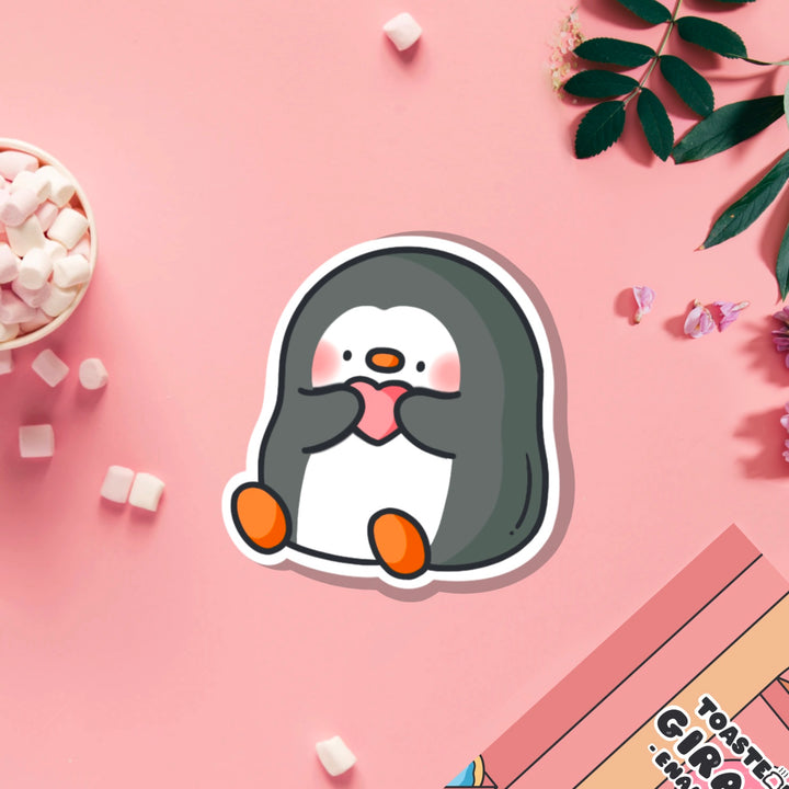 Penguin holding heart vinyl sticker on pink table