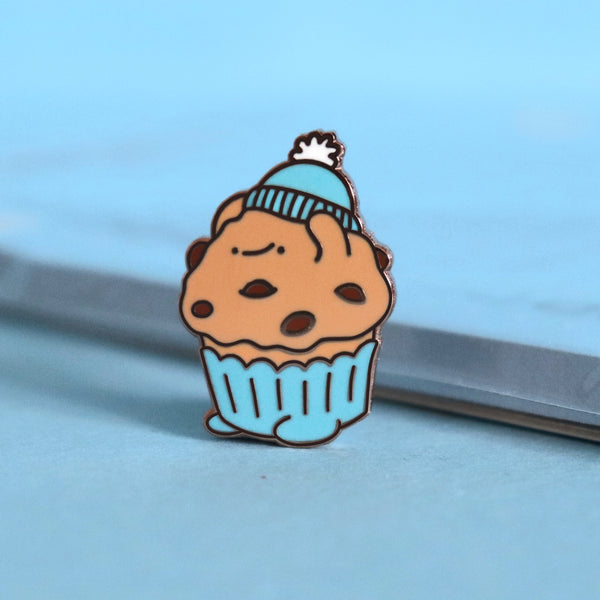 Muffin enamel pin on blue table with notepad