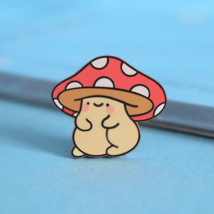 Mushroom enamel pin on blue table with notepad