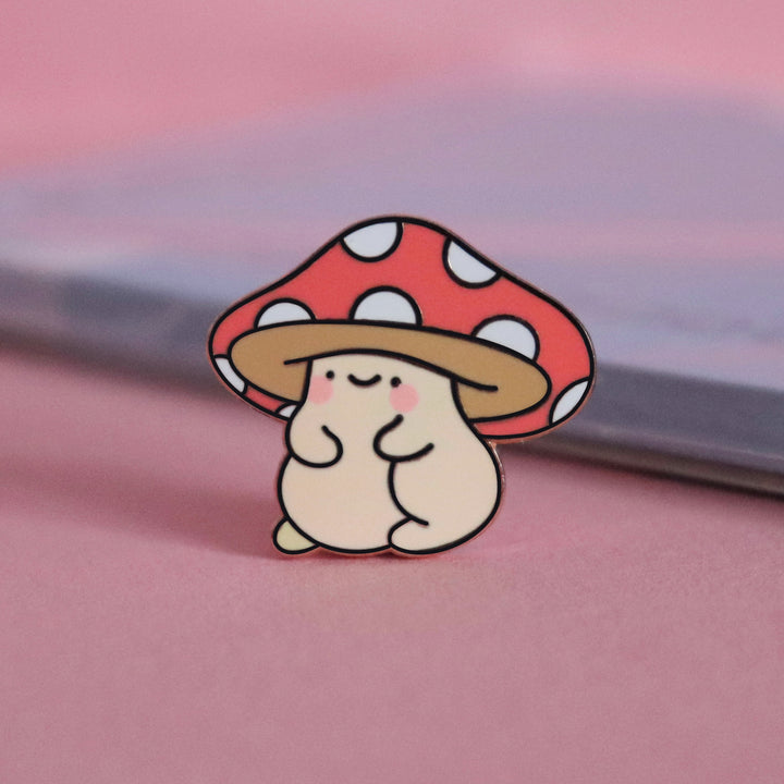 Mushroom enamel pin on pink table with notepad