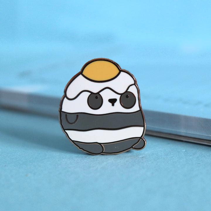 Panda with an egg on his head enamel pin on blue table with notepad