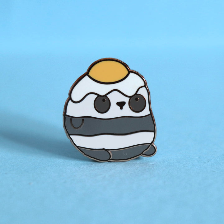 Panda with an egg on his head enamel pin on blue table