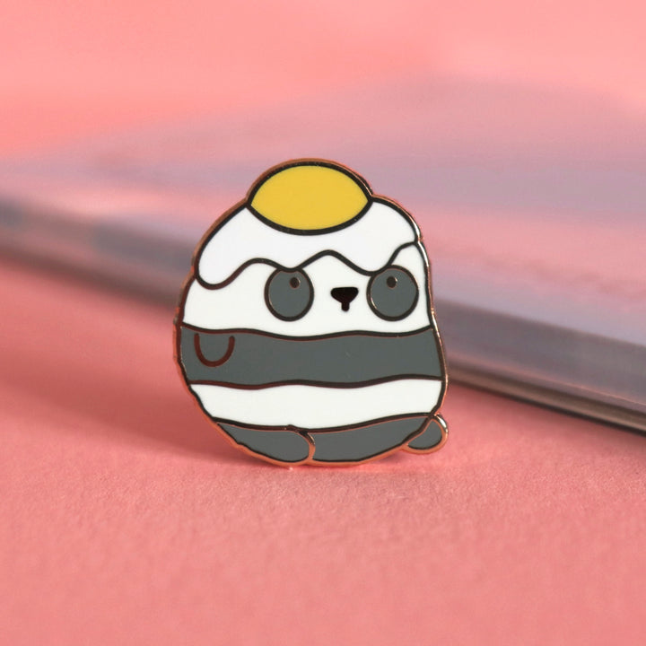 Panda with an egg on his head enamel pin on pink table