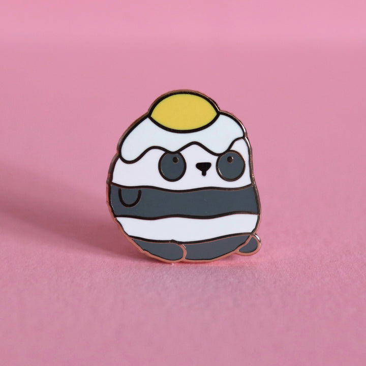 Panda with an egg on his head enamel pin on pink desk