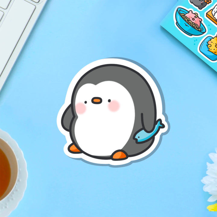 penguin holding fish vinyl sticker on blue table