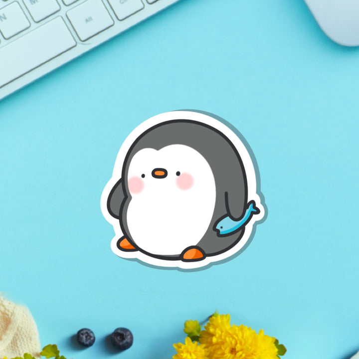 penguin holding fish vinyl sticker on table with keyboard