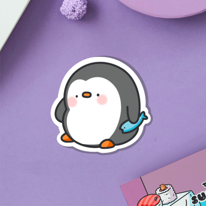 penguin holding fish vinyl sticker on purple table