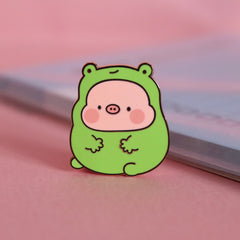 Pig in frog costume enamel pin on pink desk with notepad