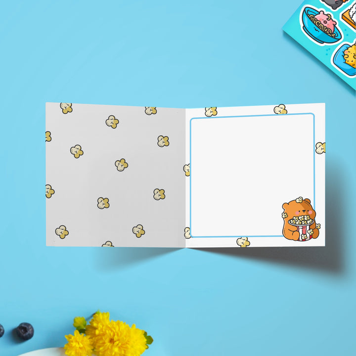 Bear with popcorn card with popcorn print inside on blue table