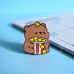 Bear with popcorn enamel pin on blue table with notepad