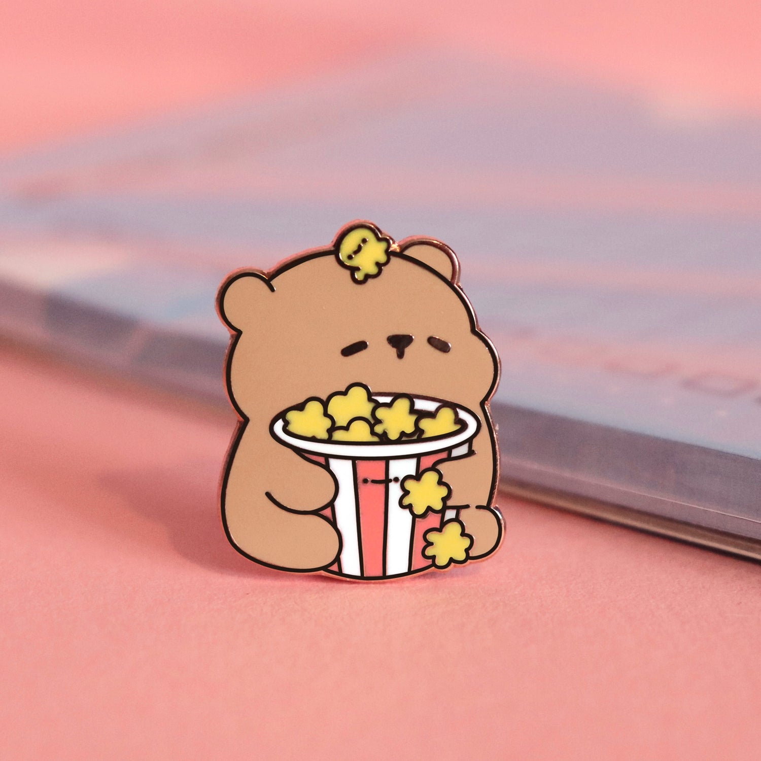 Bear with popcorn enamel pin on pink table with notepad
