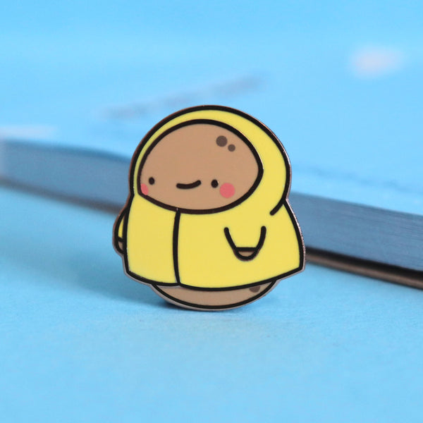 Potato in a raincoat enamel pin on blue table with notepad