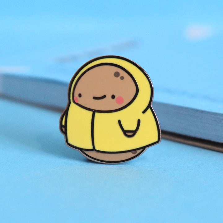 Potato in a raincoat enamel pin on blue table with notepad