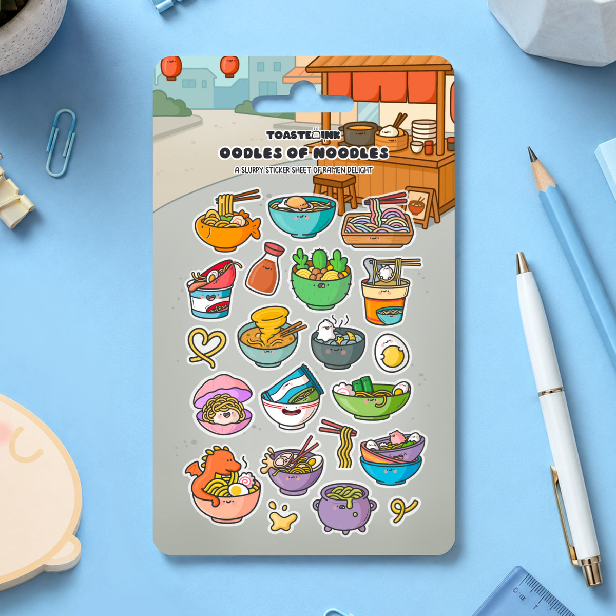 Ramen noodles sticker sheet scattered on blue desk with stationery