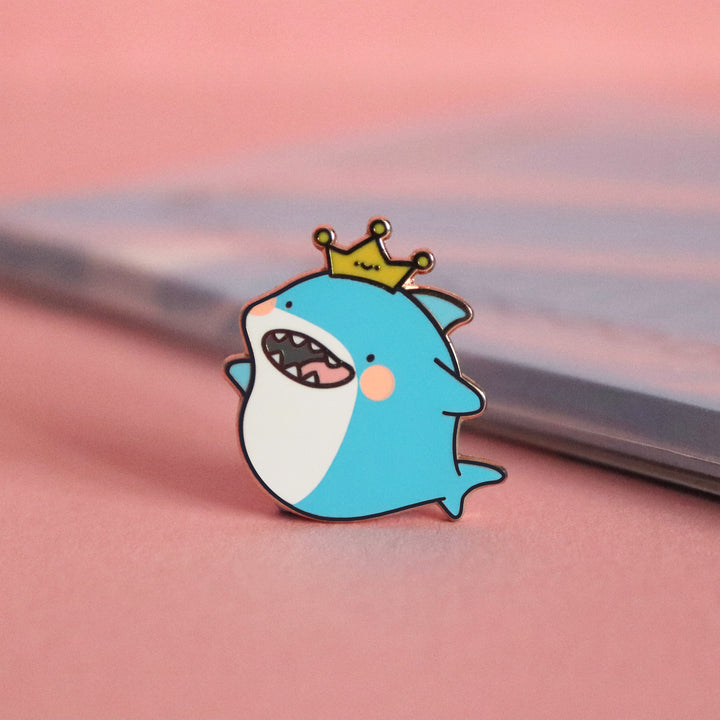 Shark enamel pin on pink table with notepad