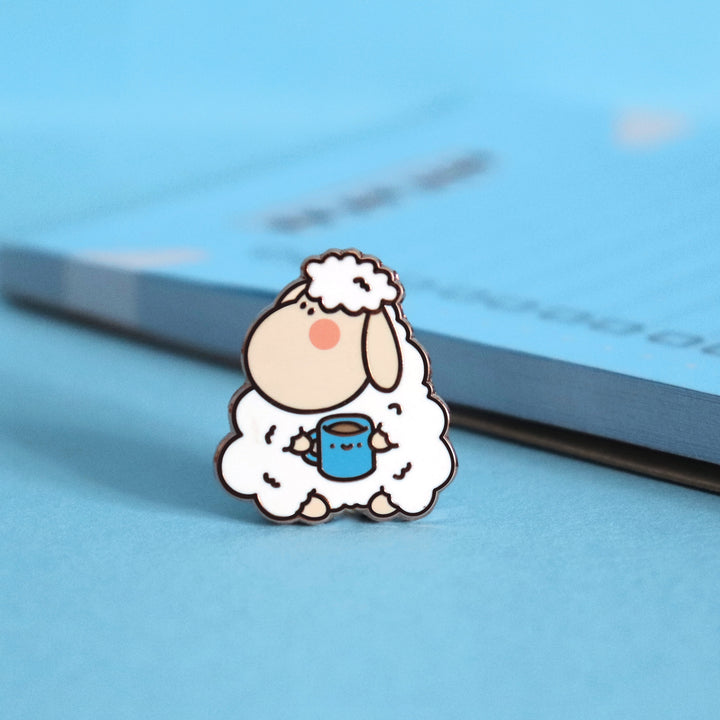 Sheep enamel pin on blue table next to notepad