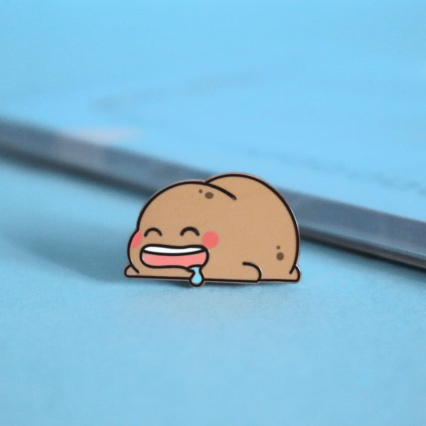 Sleeping potato enamel pin on blue table with notepad