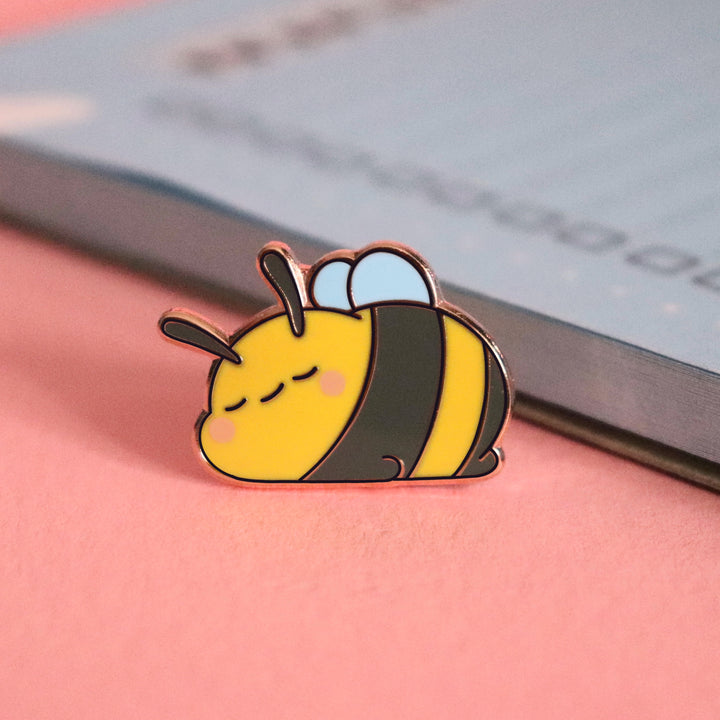 Sleeping bee enamel pin on pink desk with notebook