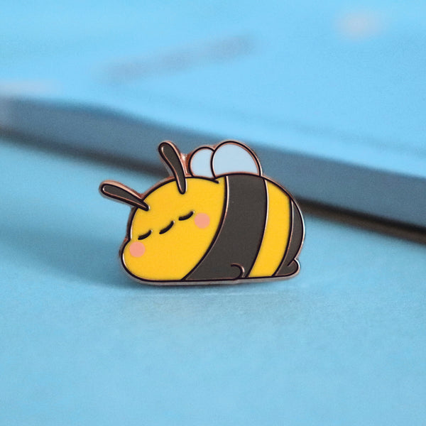 Sleeping bee enamel pin on blue table with notepad