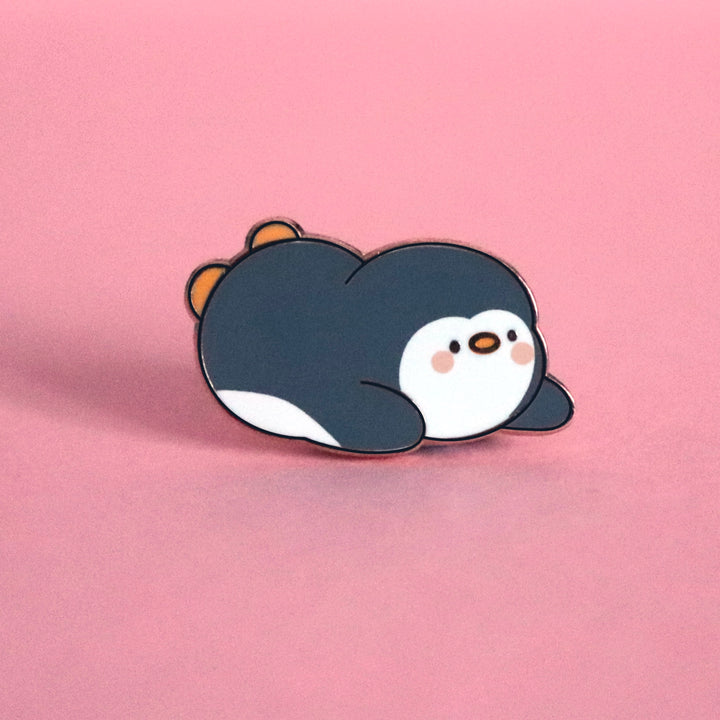 Penguin sliding on his belly enamel pin on pink table