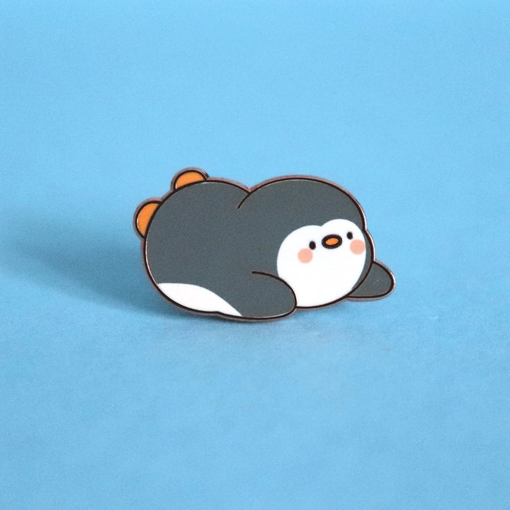 Penguin sliding on his belly enamel pin on blue desk