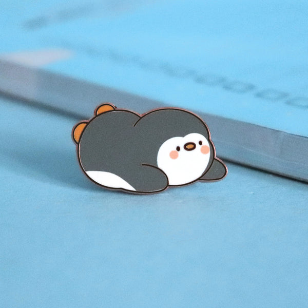 Penguin sliding on his belly enamel pin on blue table with notepad